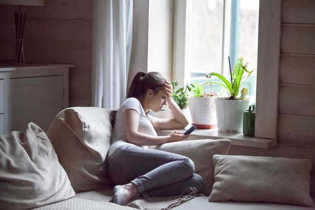 a sad woman is lying on her bed while using her phone