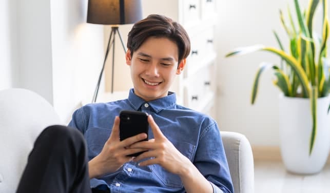 a happy guy in a blue shirt is using his smartphone and smiling