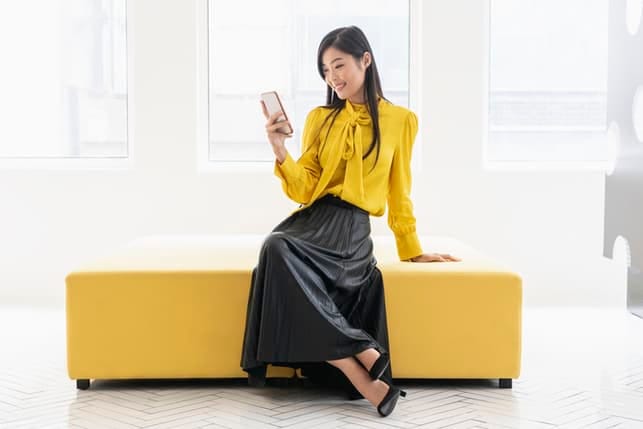 a young Asian woman in yellow using her smartphone