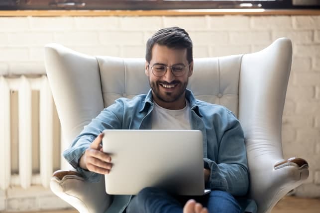 an attractive dark man in a blue shirt is using his laptop and smiling