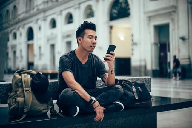 a young asian man in black is checking his phone in the city
