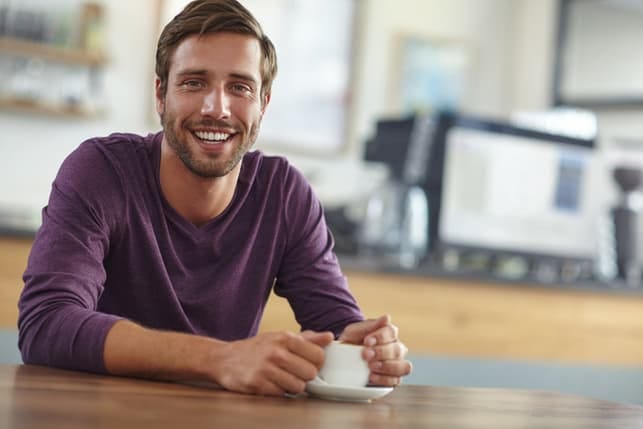 a young smiling guy posing while holding a cup of tea