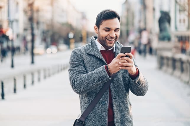 a man is checking his phone while smiling outdoors