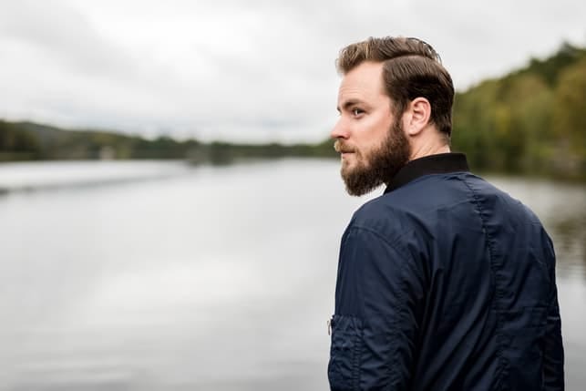 a handsome bearded man in a black shirt posing outdoors
