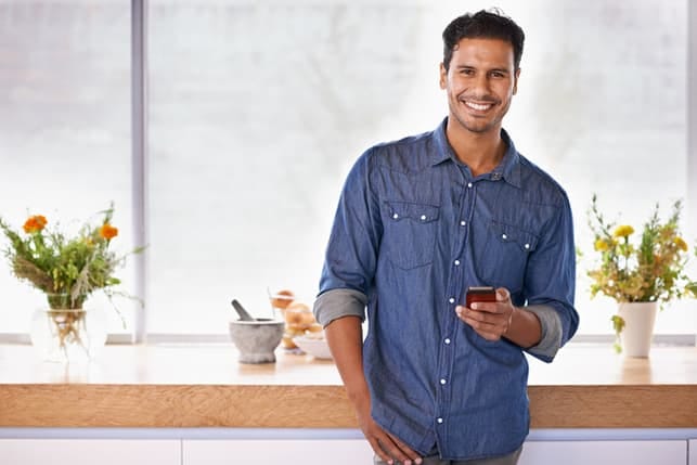 a man in a blue shirt posing in the kitchen while holding a smartphone in his hands