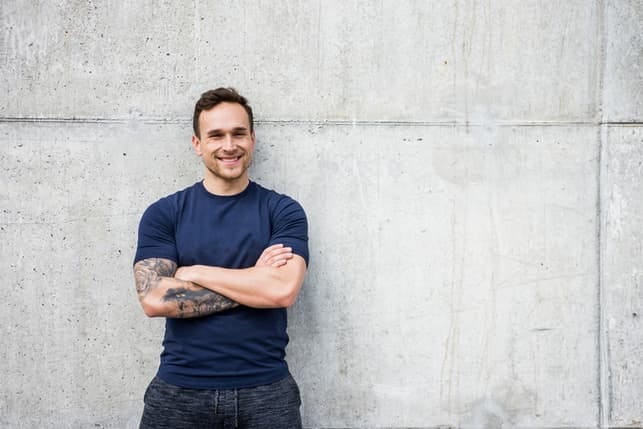 a portrait of a man with an arm tattoo wearing a blue T-shirt