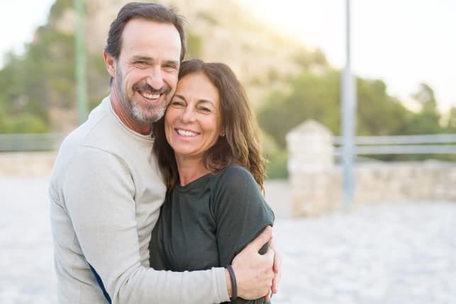 a mature couple is hugging and smiling while posing outside