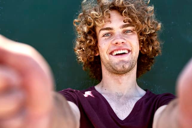 a young man with curly hair is smiling and taking a selfie