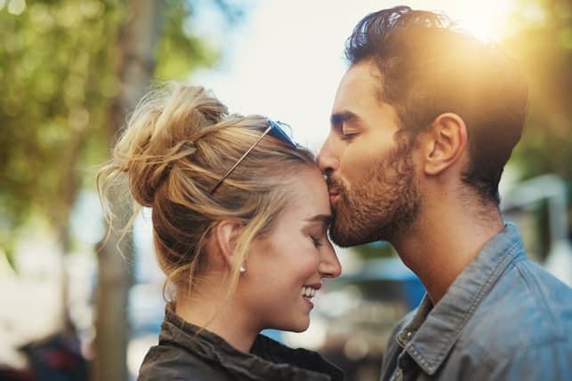 a man kissing his girlfriend’s forehead outdoors