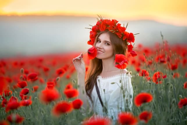 a woman is smelling flowers while sitting on the ground in the field