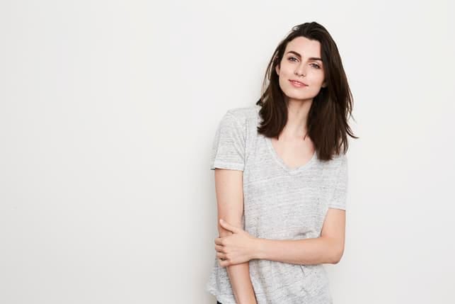 a portrait of a young dark-haired woman in a grey T-shirt posing on a light grey background